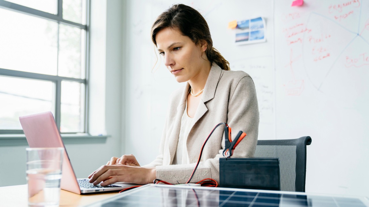 Eine Frau arbeitet am Schreibtisch mit dem Laptop und informiert sich über aktuarielle Gutachten
