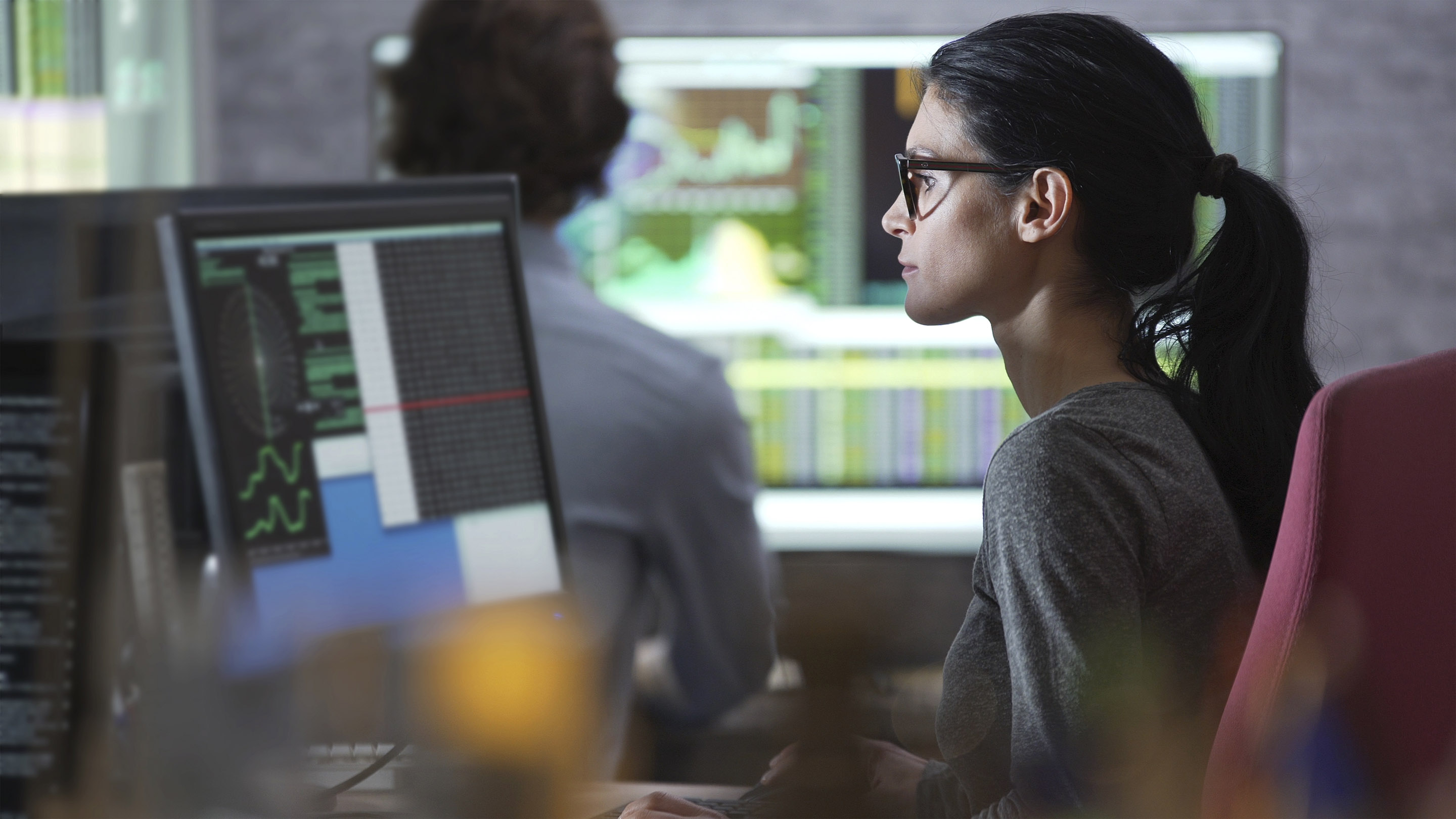Stock photo of a good looking man &  woman working in an office surrounded by large computer monitors.