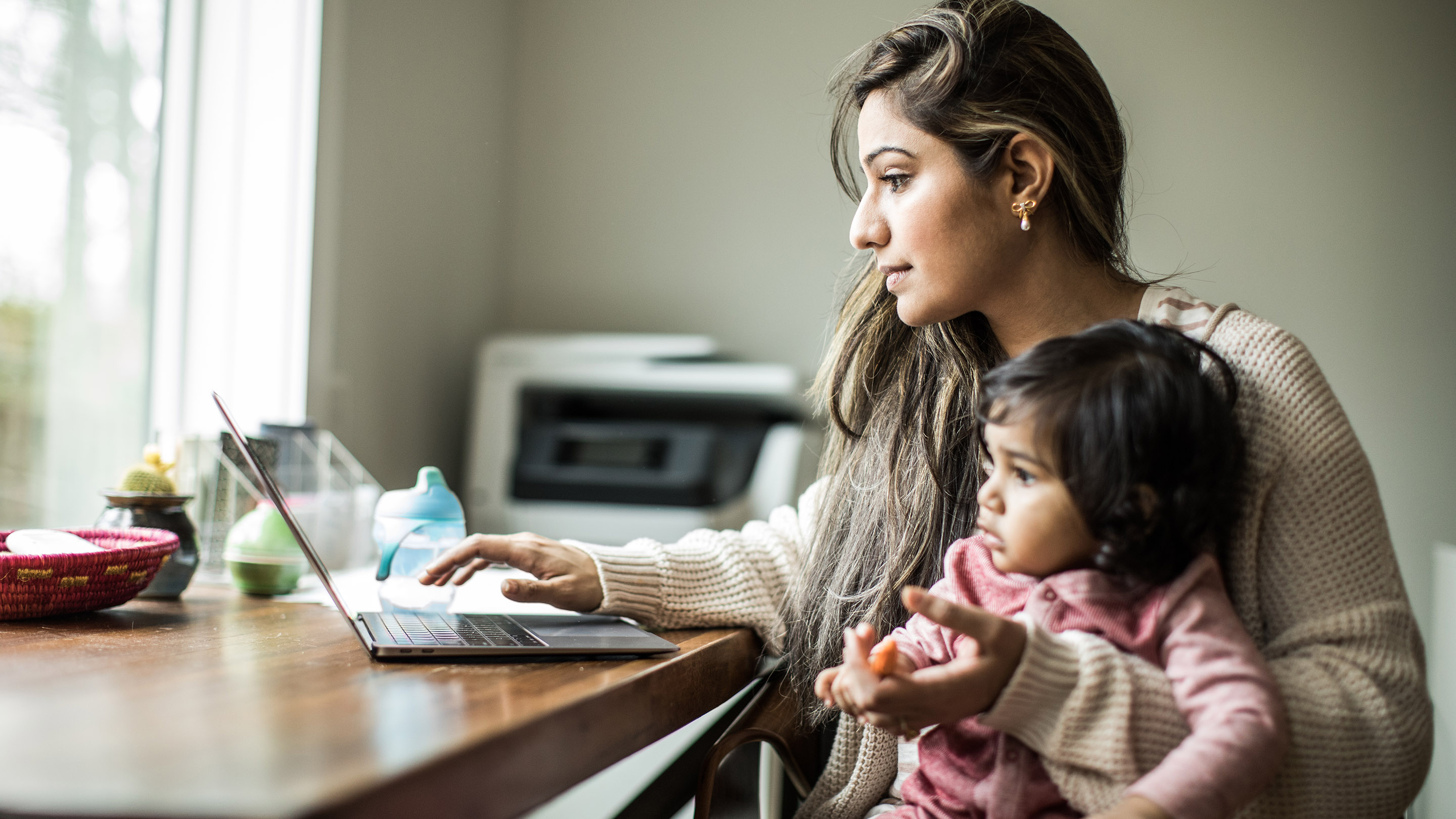 Mother multi-tasking with infant daughter in home office