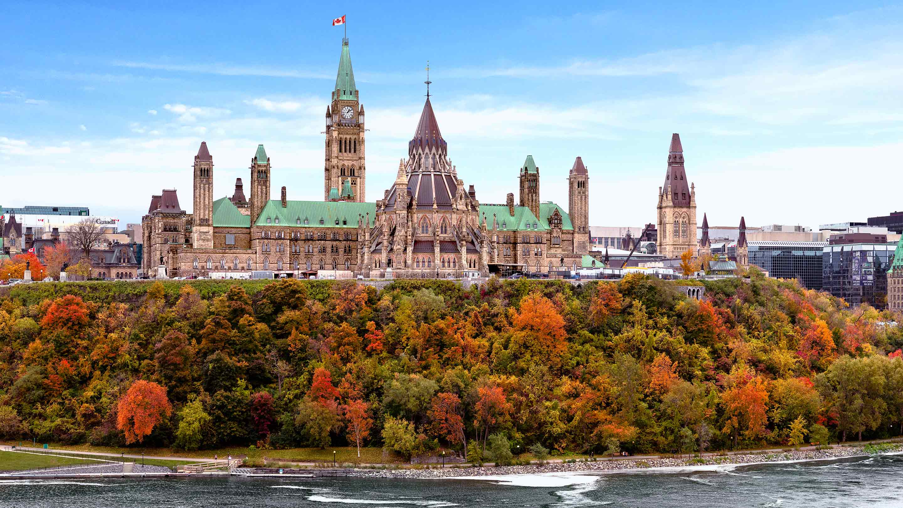 La Colline du Parlement présente de superbes couleurs automnales alors que les feuilles vibrantes contrastent avec l’architecture historique. La rivière des Outaouais s’écoule doucement à proximité, améliorant le paysage pittoresque.