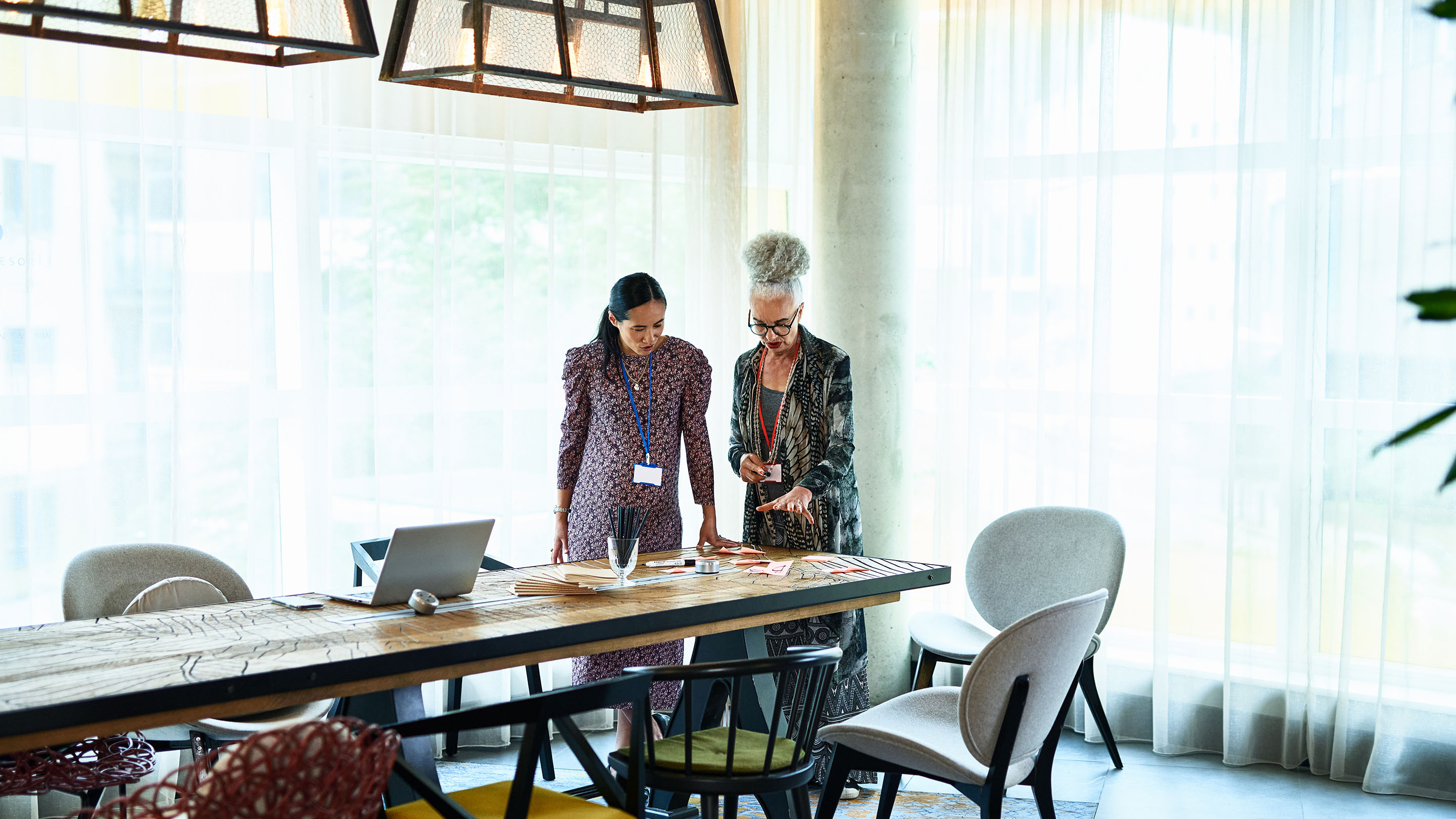 Two businesswomen standing by table and discussing ideas, collaboration, teamwork, creativity