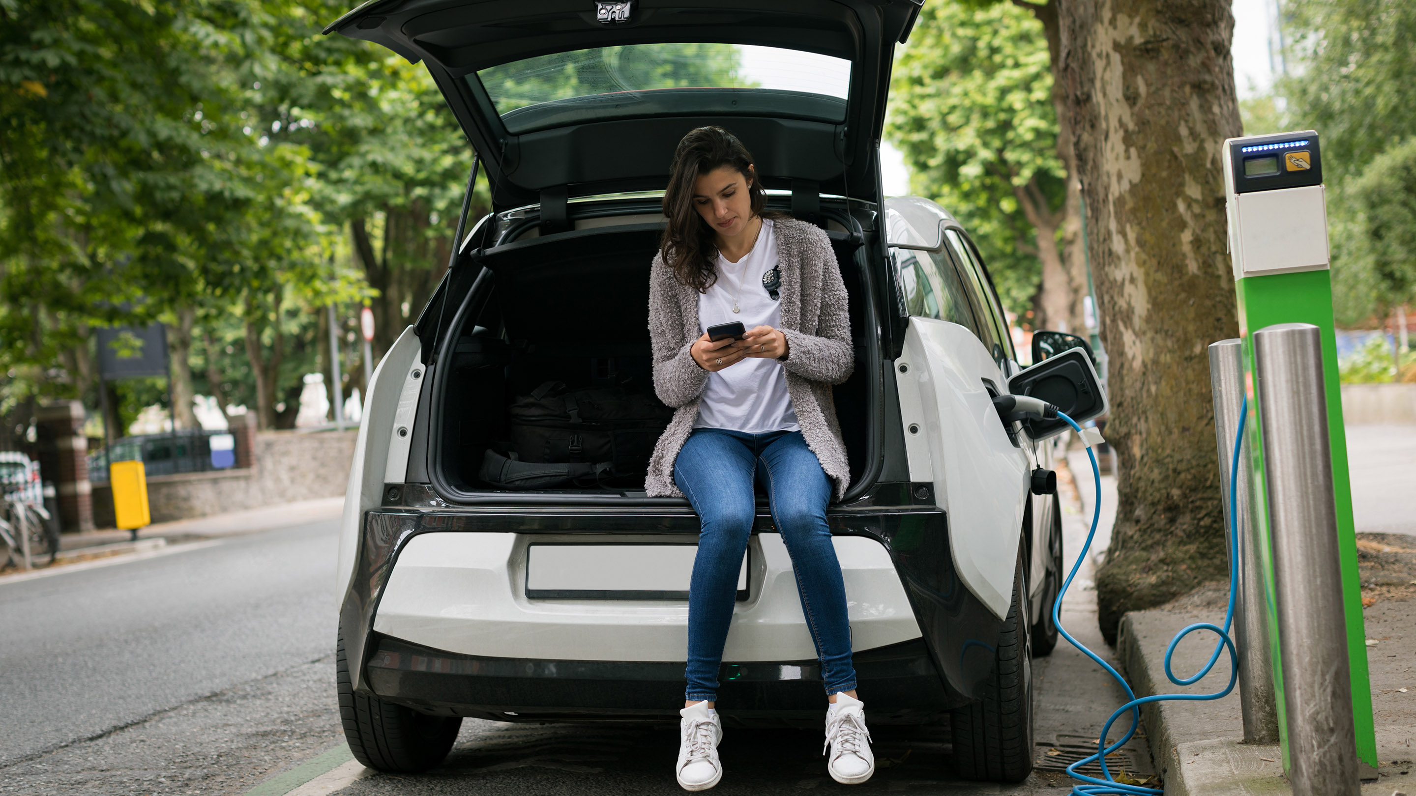 Woman using mobile phone while charging electric car at charging station