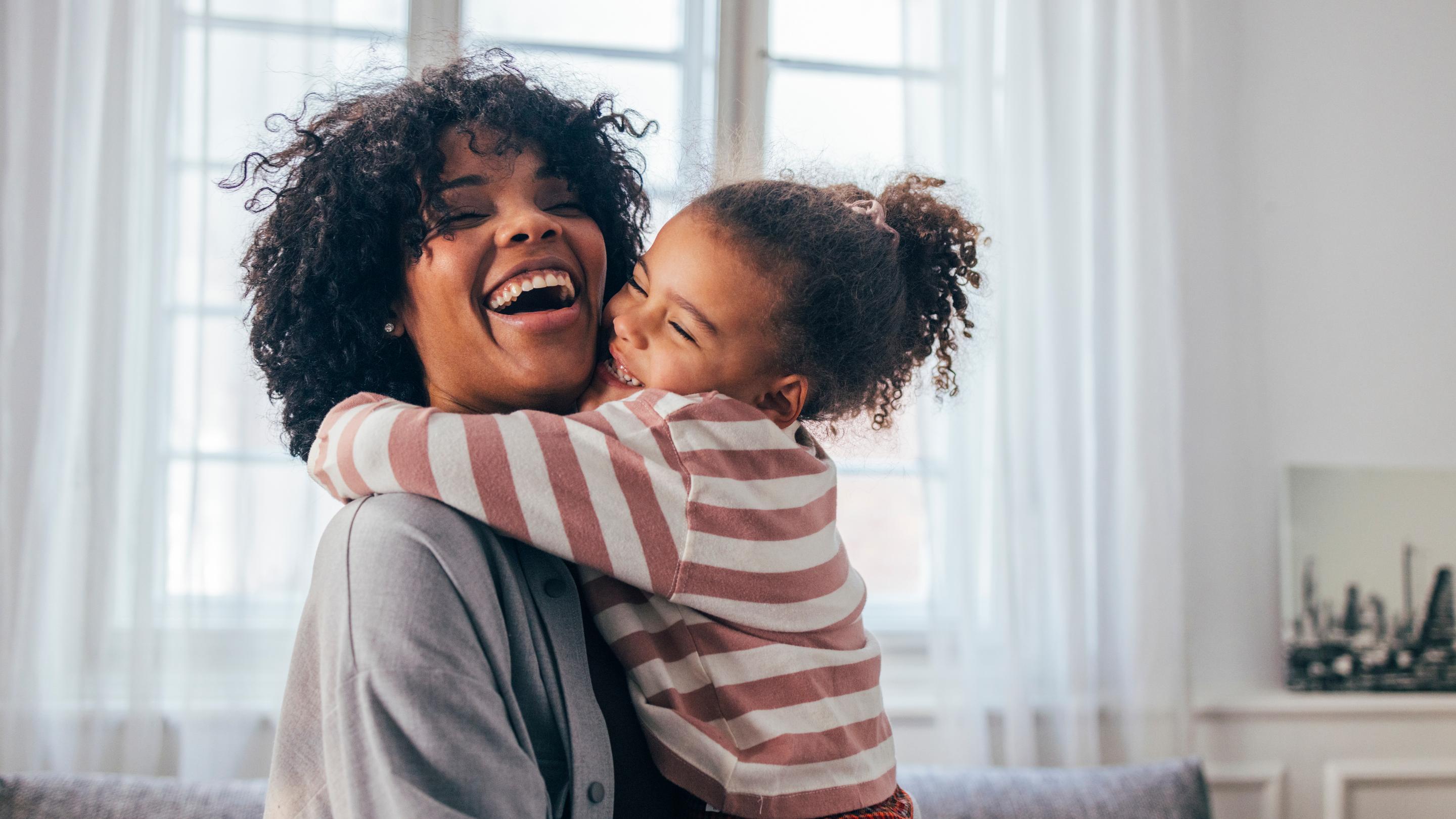 A child embraces a woman while both smile and laugh