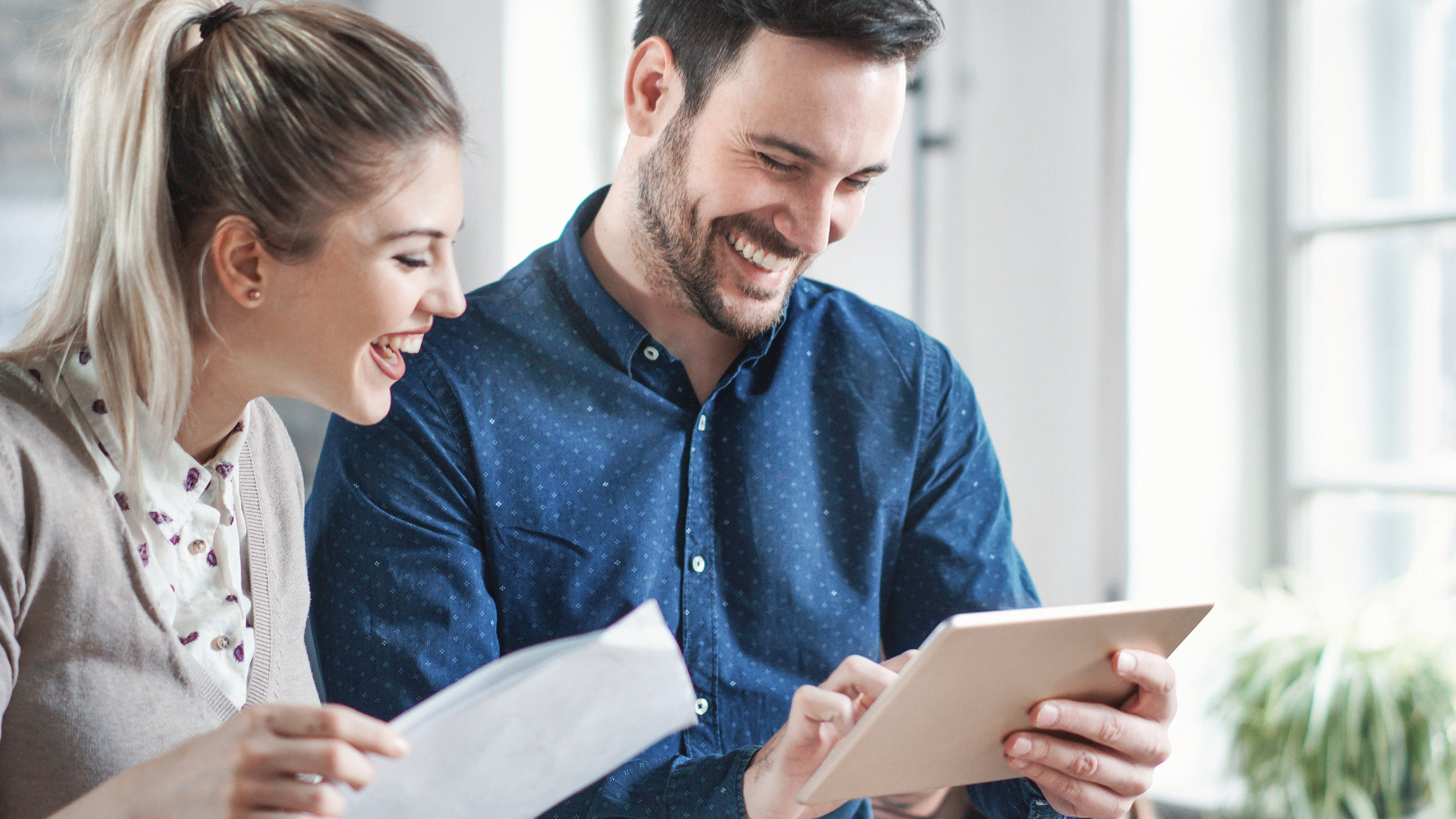 Closeup of mid 20's man and woman using a digital tablet during their break at the office. They are watching some funny content on social media websites.