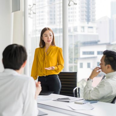 Confident businesswoman giving presentation in board room. Professionals are in meeting at conference table. They are sharing ideas in office.
