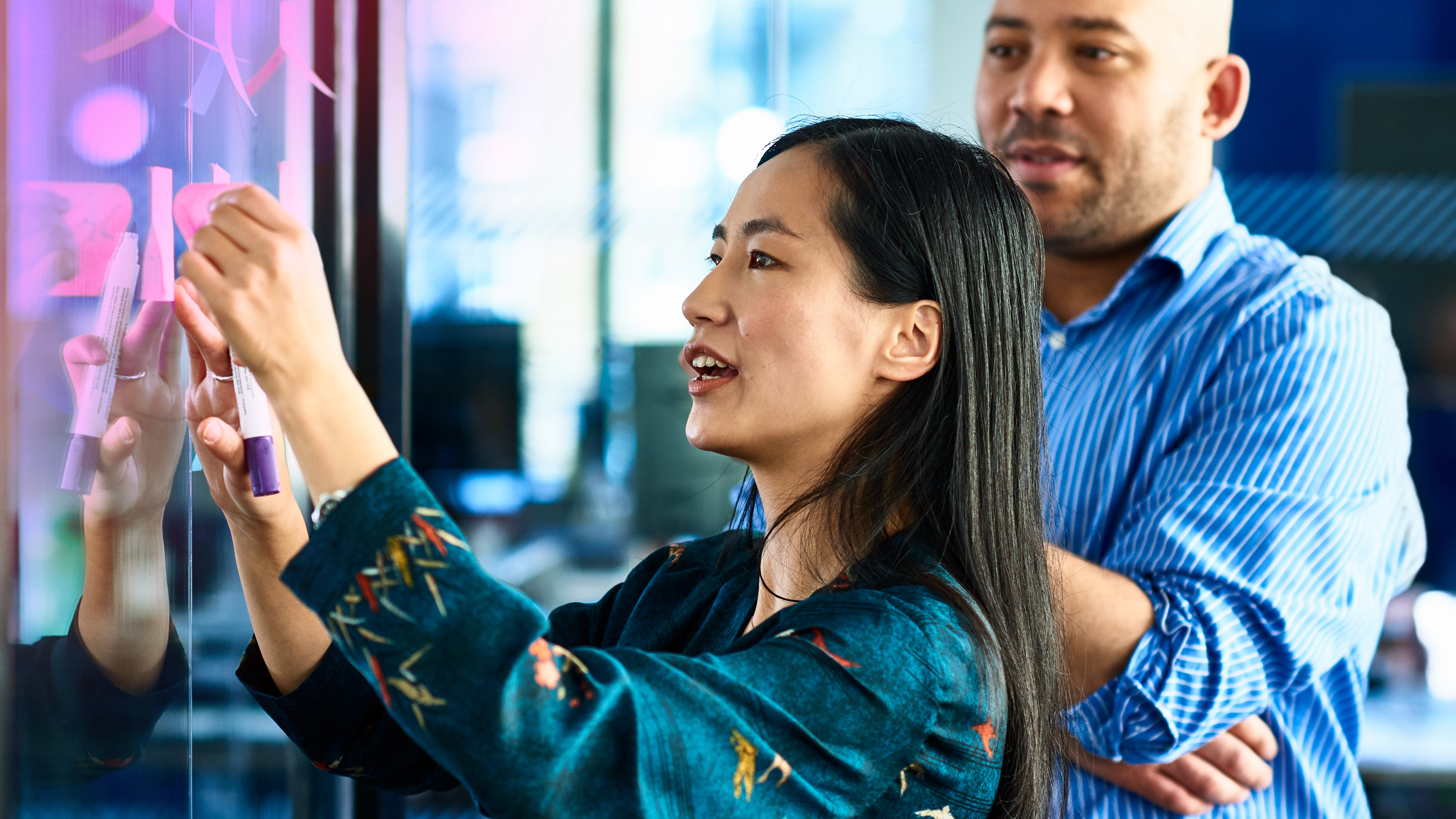 Chinese businesswoman sticking notes on glass with colleague