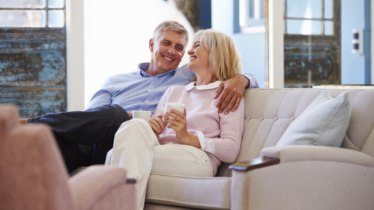Ein älteres Paar sitzt lächelnd auf der Couch und freut sich über seine gute betriebliche Vorsorge