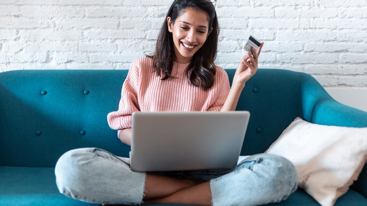 Frau die auf dem Sofa am Laptop sitzt und lacht