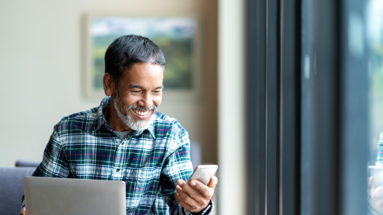 Senior Asian using tablet and mobile phone to check data, smiles, happy and positive. 