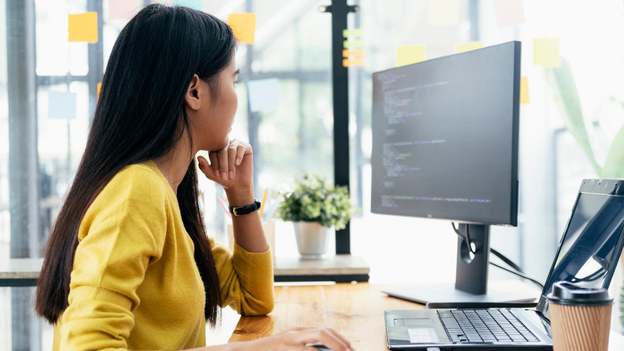 Woman sitting at a desk working on a computer next to a large window.