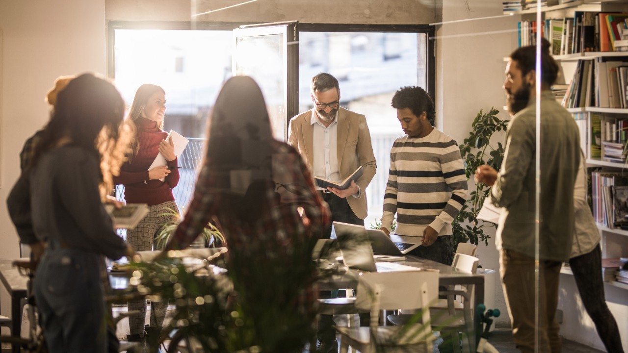 Group of multi-tasking creative people working on a meeting in the office. The view is through glass.