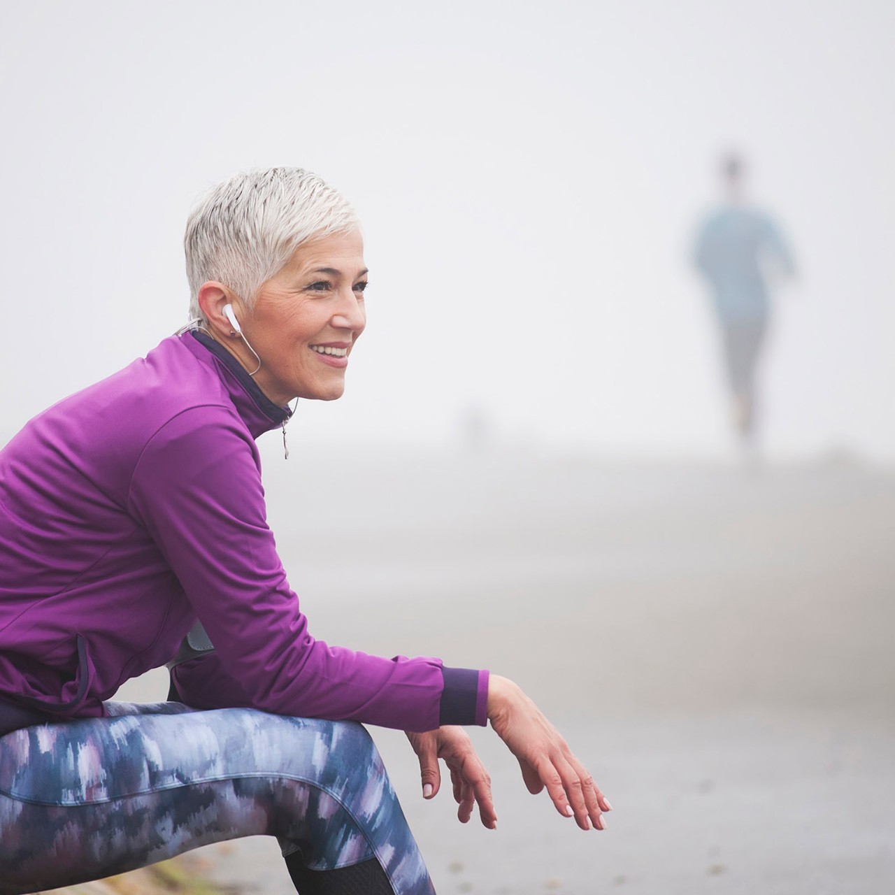 Beautiful mature woman jogging through fog in early autumn day