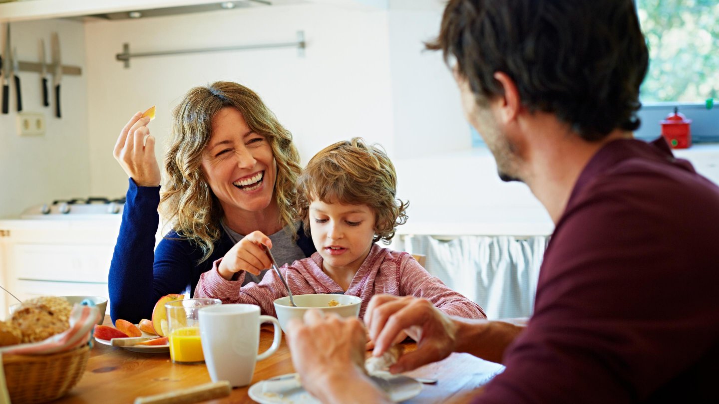Happy family of three enjoying breakfast at table in domestic kitchen.