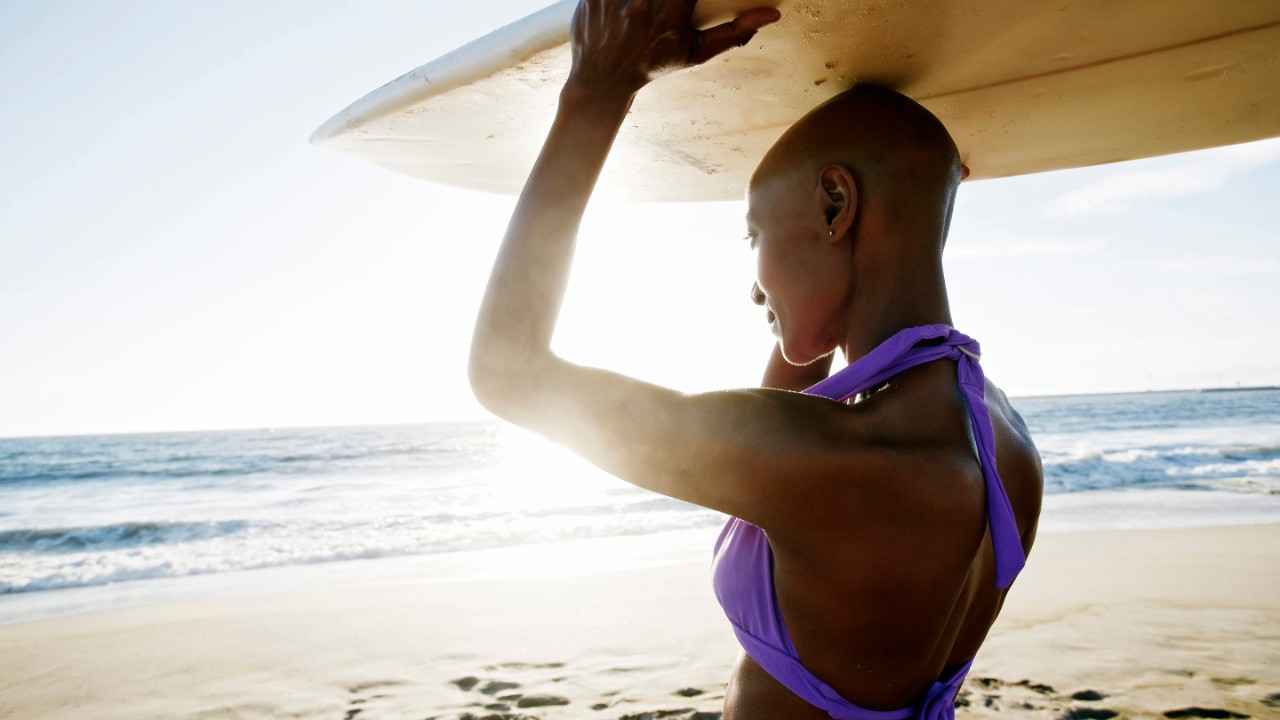 Black woman carrying surfboard on beach