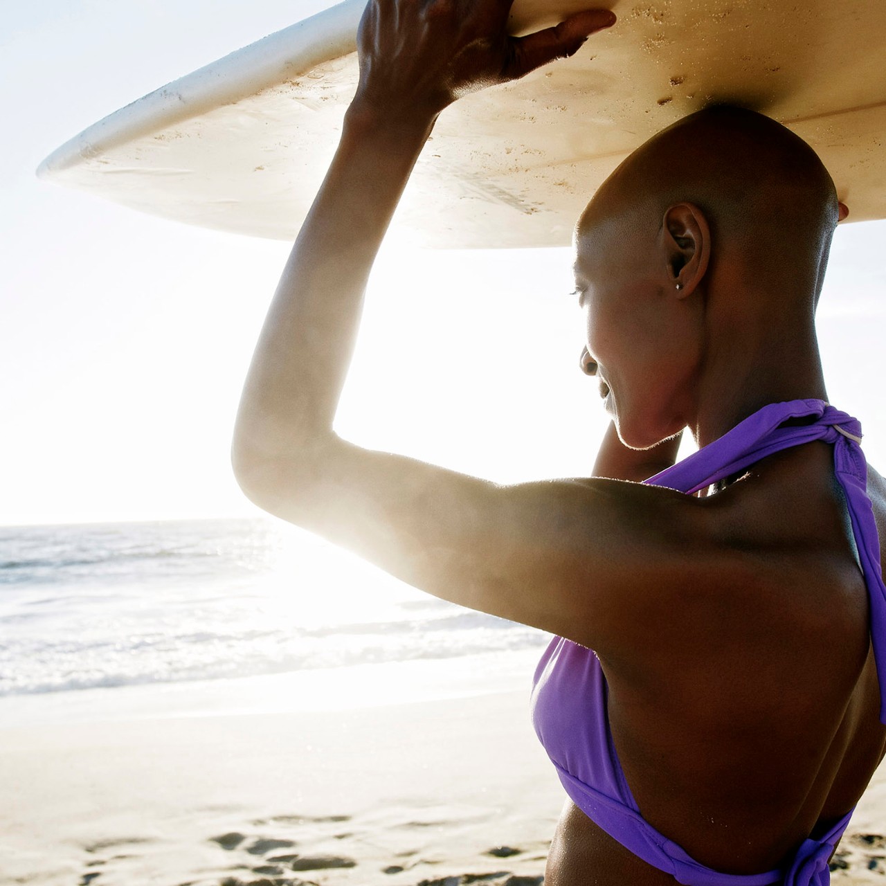Black woman carrying surfboard on beach