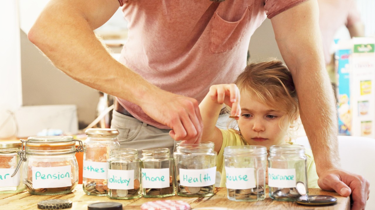 Young girl and father putting money into savings jars