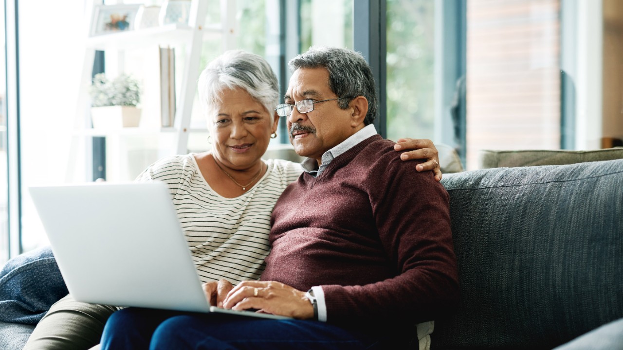 senior couple using laptop, sat on sofa