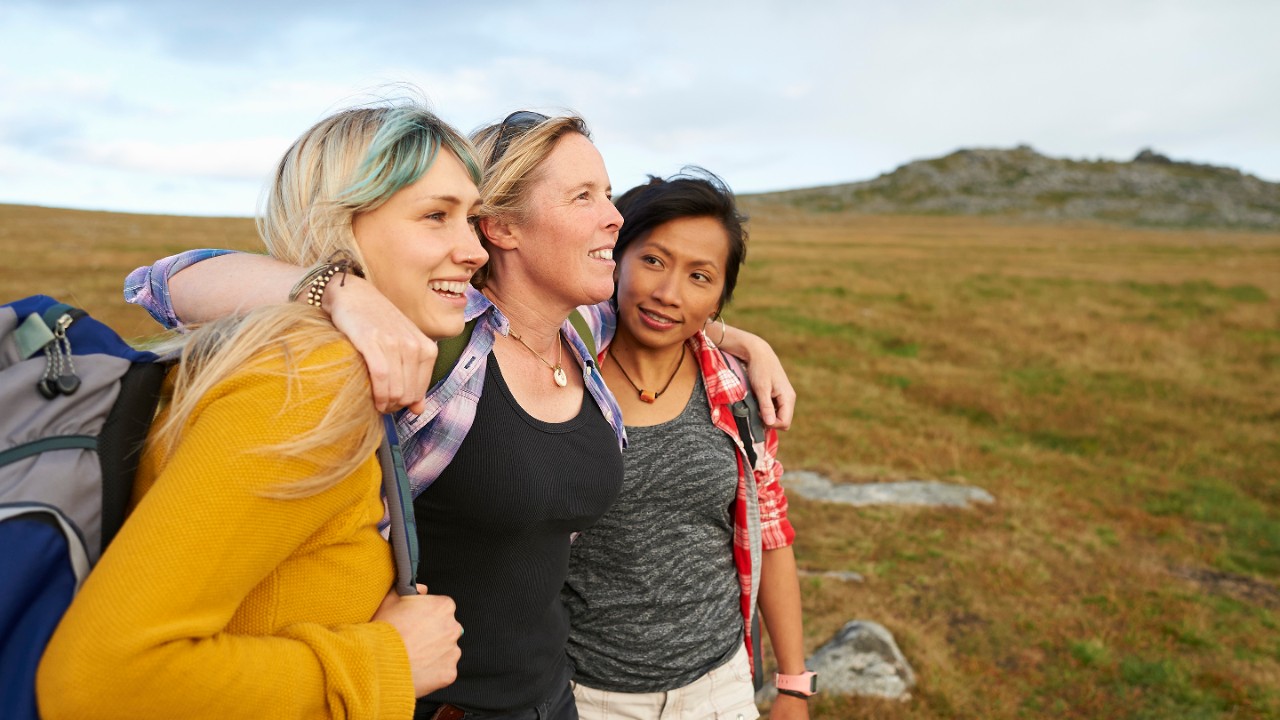 A group of happy and positive female hiking friends huddle together on a rocky moorland in an idyllic rural countryside.