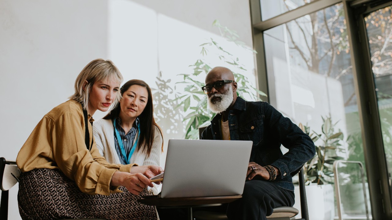 two woman and a man - sit around a laptop