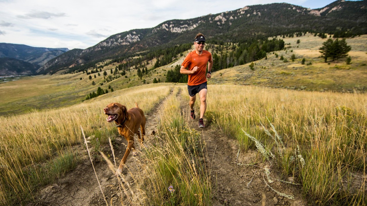 A man Trail running in Big Sky with his dog