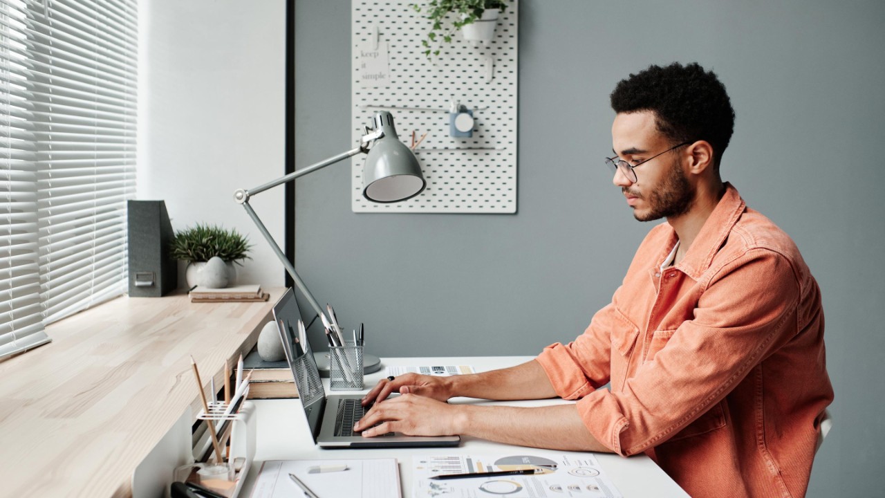 Serious busy young black marketing specialist in eyeglasses working with laptop in minimalistic office.