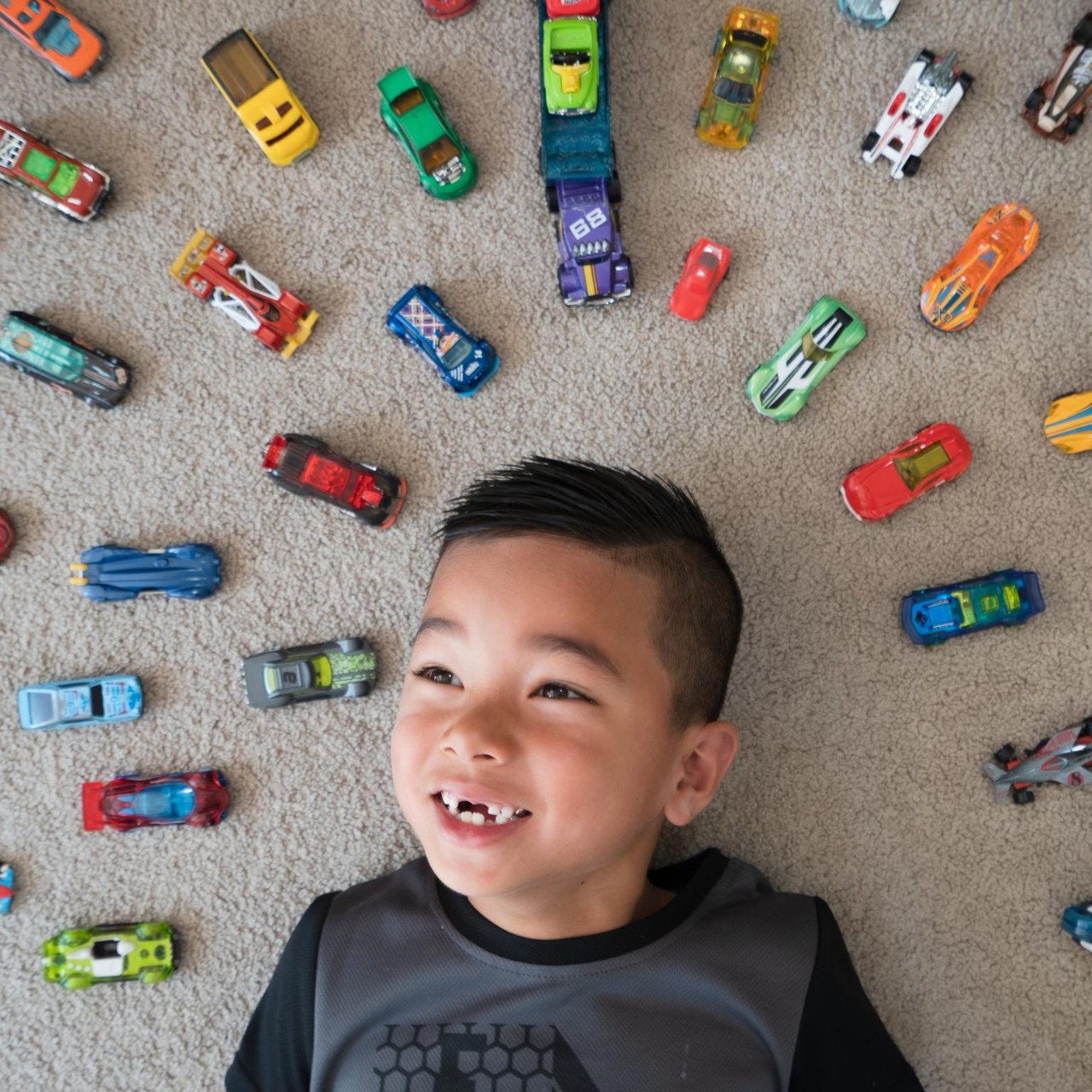 Kid at home lying on ground with cars around him