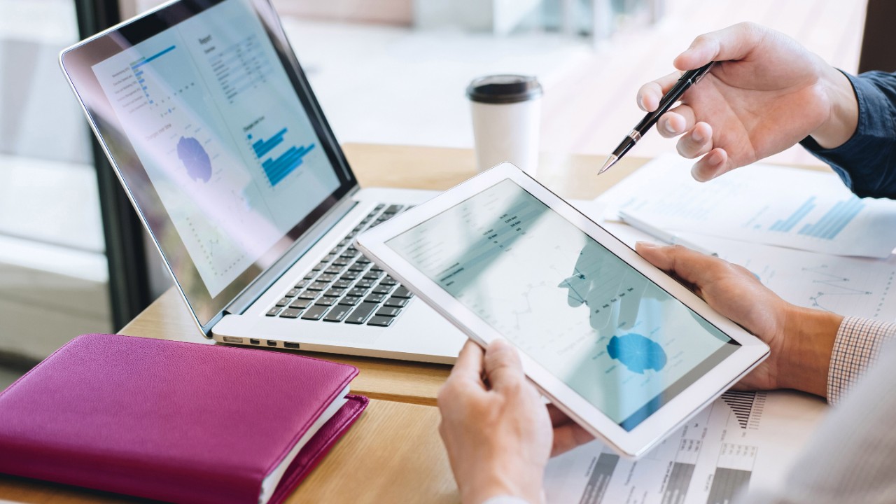 Midsection Of Businessman Holding Digital Tablet Discussing With Colleague At Desk In Office
