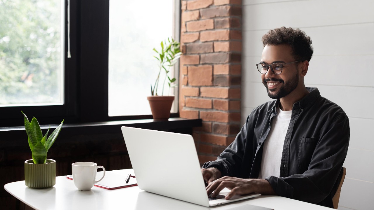 Black man smiling in casual office, on laptop