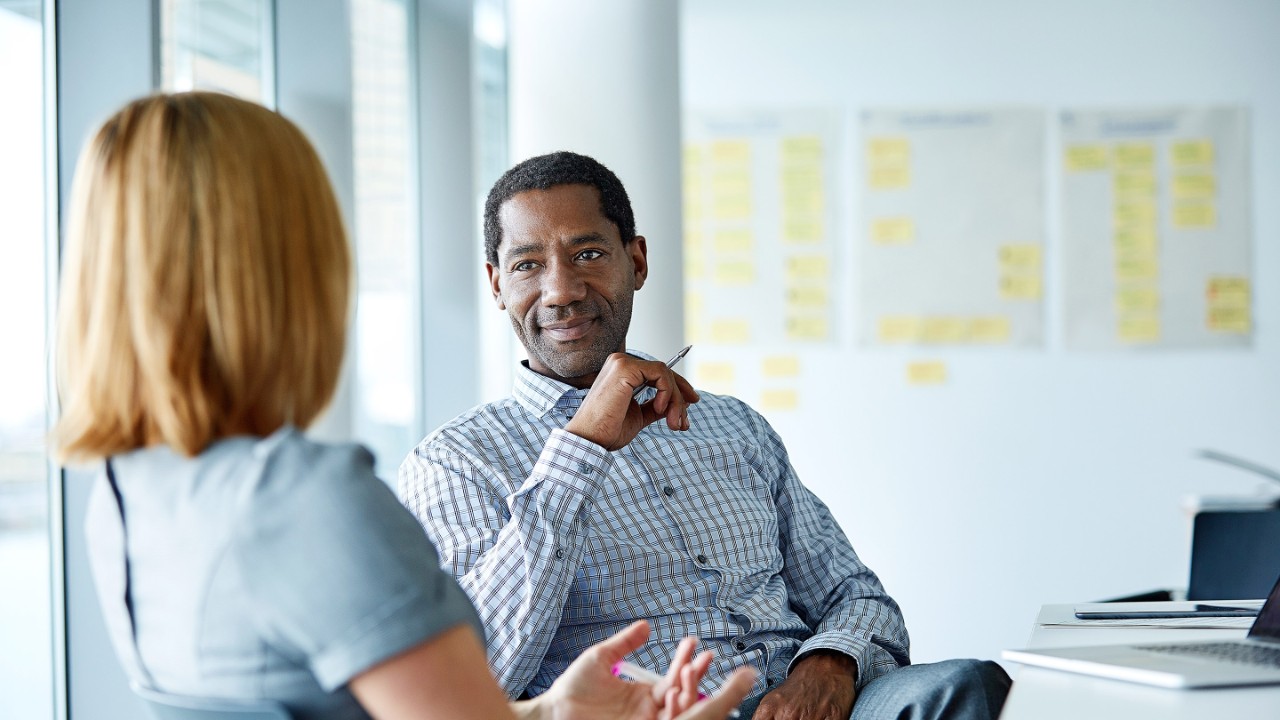 Shot of two colleagues talking together whilst sitting in a modern office