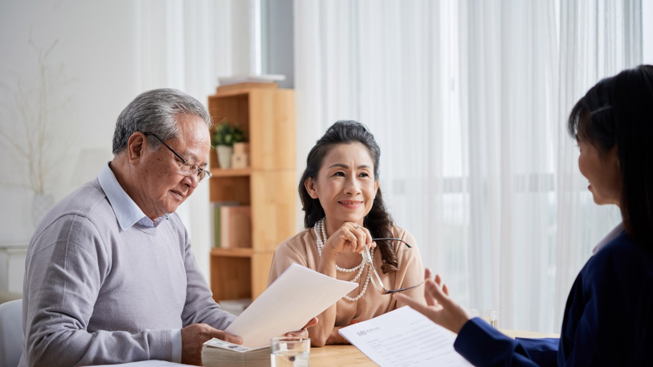 Man and woman sat at desk with adviser reviewing papers