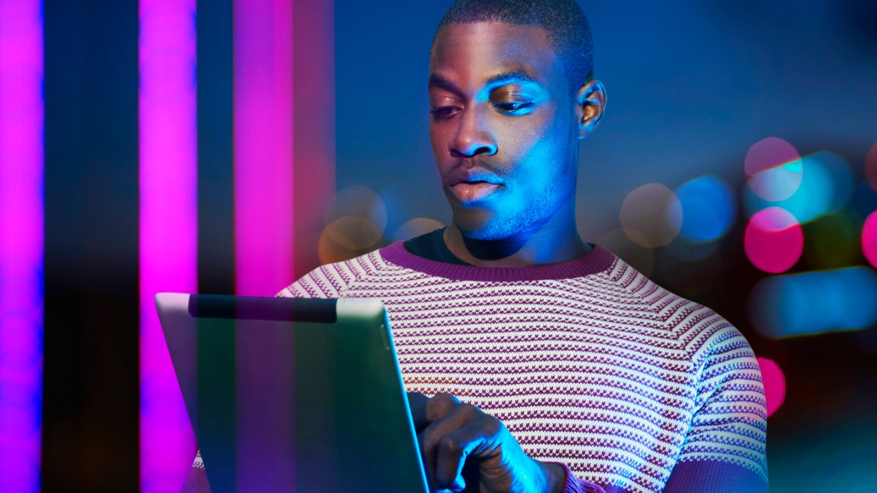 Young black man on tablet with pink neon lights in the background