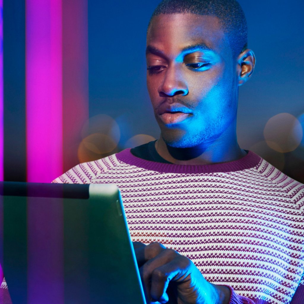 Young black man on tablet with pink neon lights in the background