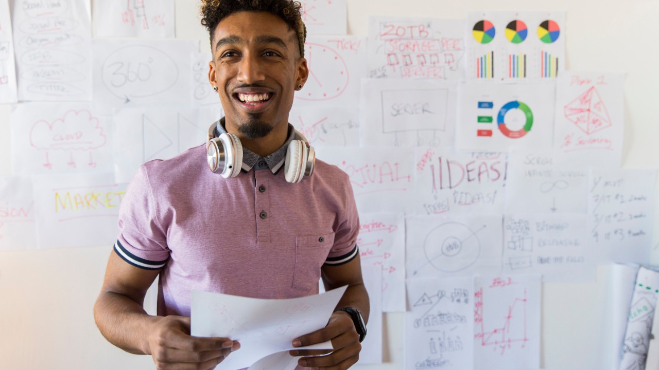 Portrait smiling, confident creative businessman hanging paperwork on office wall