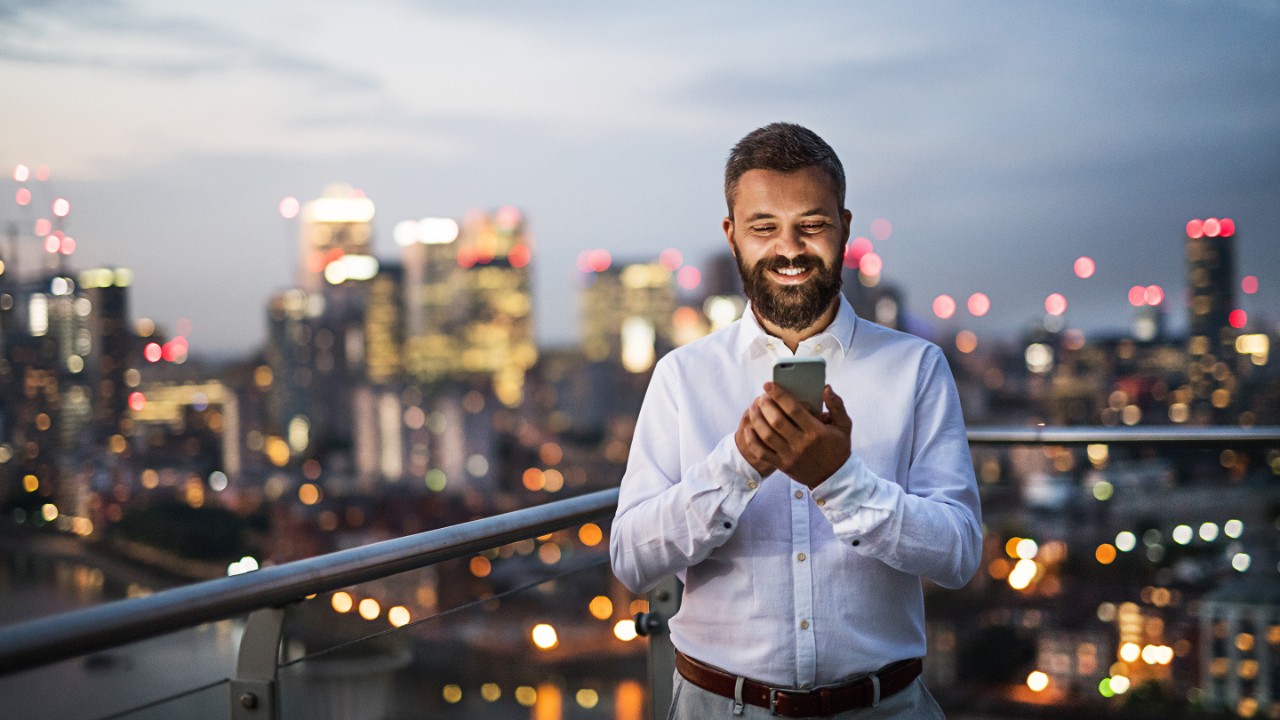 A businessman with smartphone standing against night London view panorama.