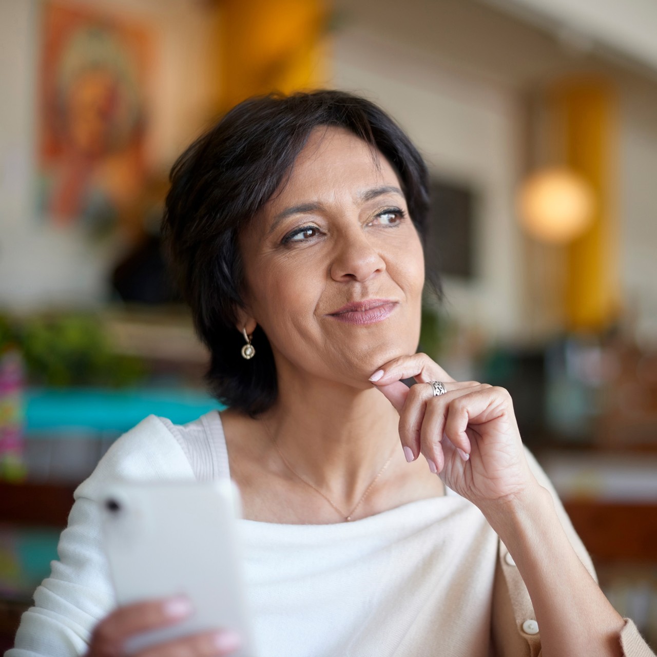 Phone, thinking and happy woman in cafe, restaurant or shop online review, social media or post ideas. Mature, Indian person on smartphone or cellphone with smile for customer service, e commerce app