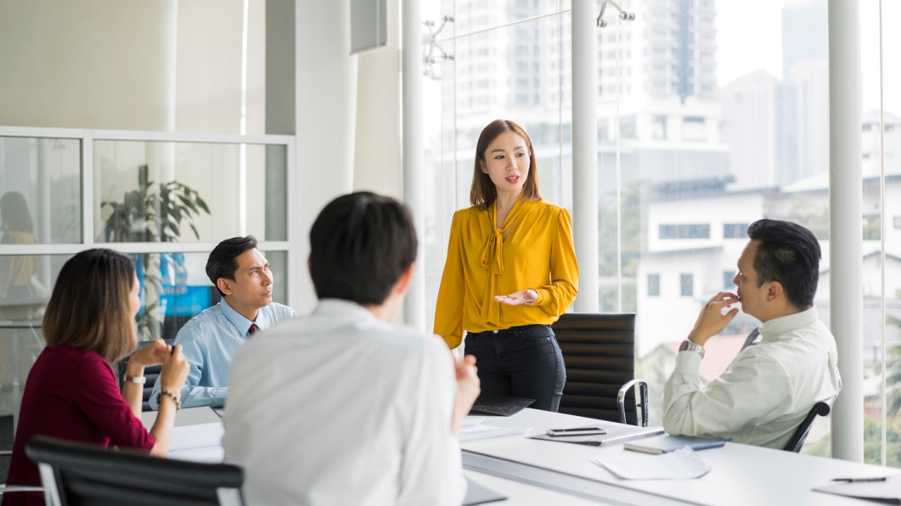 Confident businesswoman giving presentation in board room. Professionals are in meeting at conference table. They are sharing ideas in office.