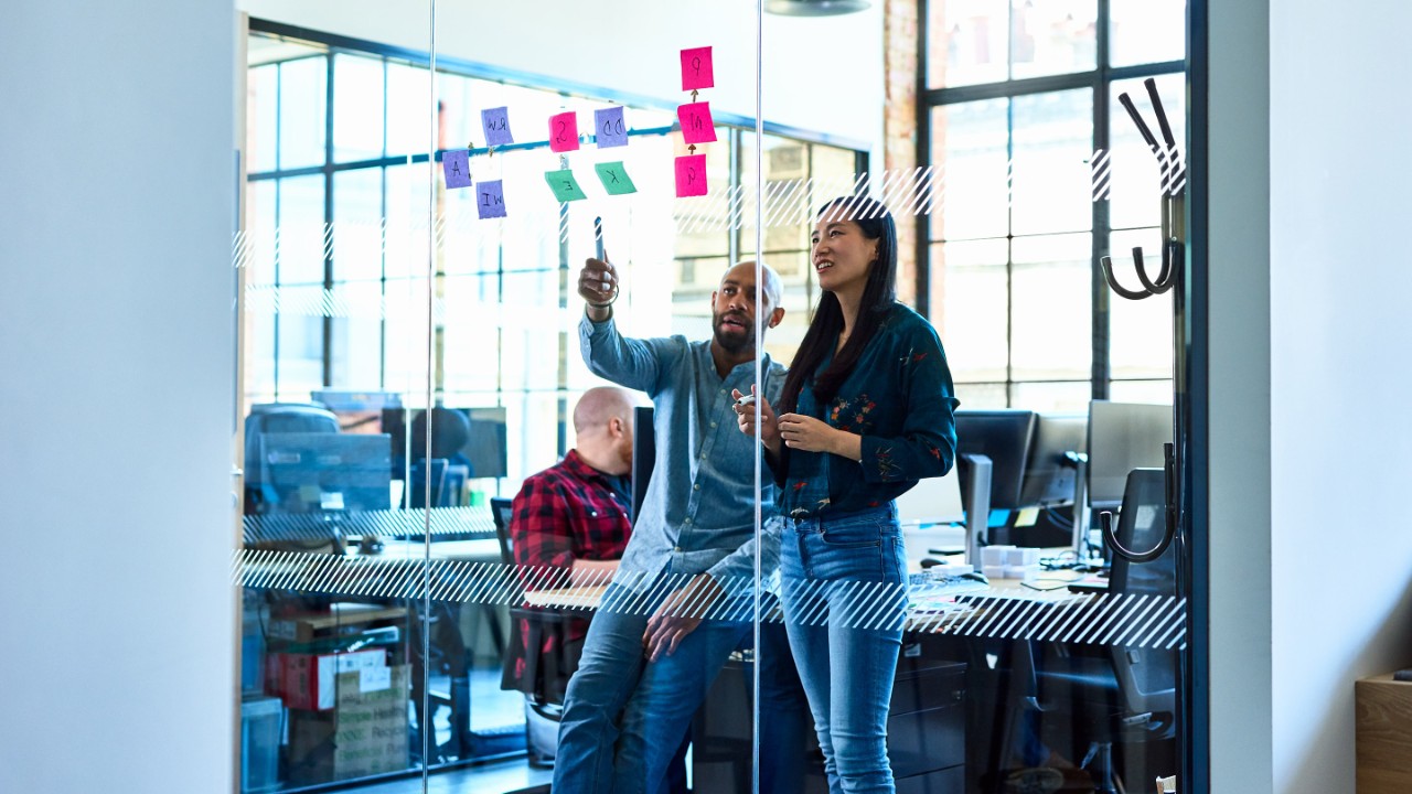 Businessman mentoring female colleague, discussing business strategy, using sticky notes to plan and solve problems, brainstorming, innovation