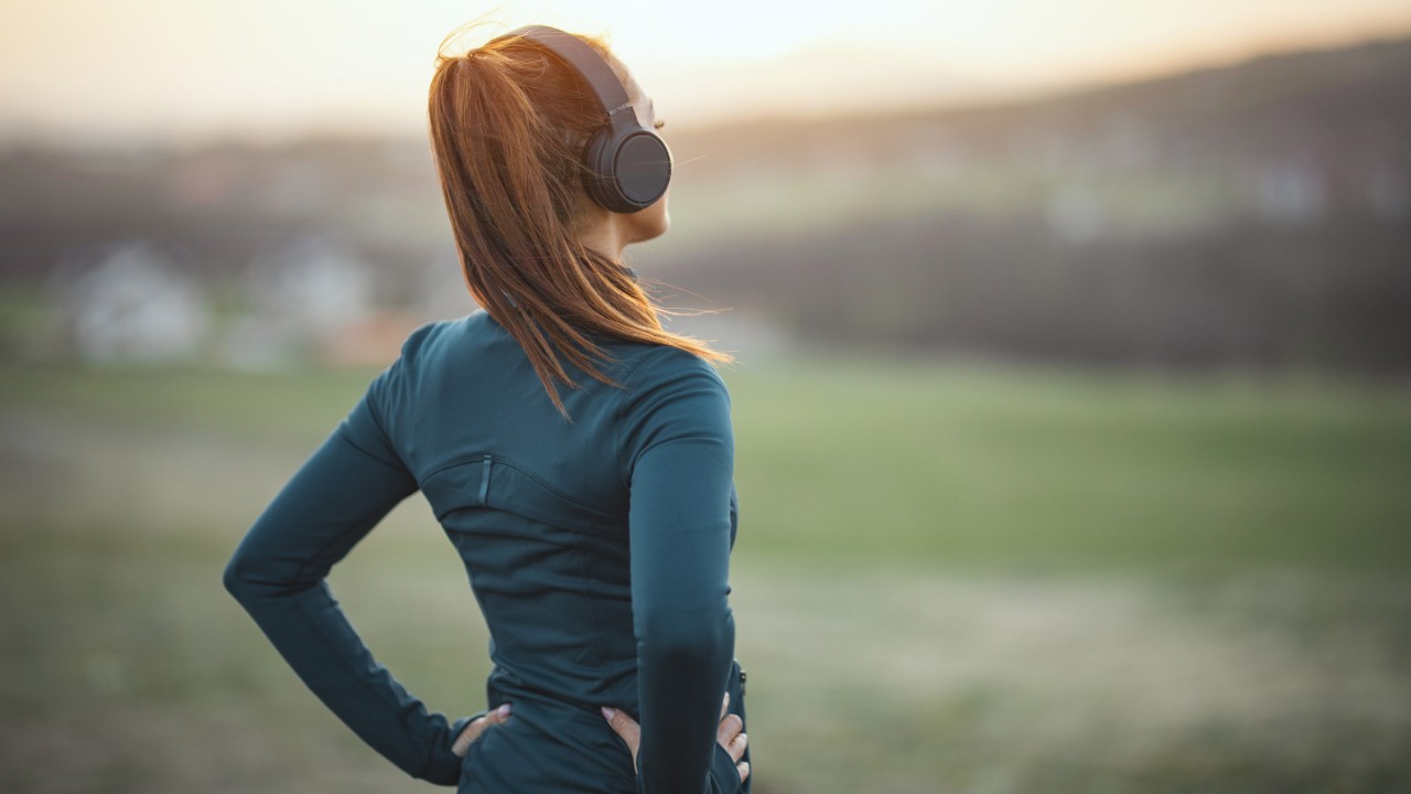 Young beautiful female runner listening to music and preparing to jogging in mountains. Rear view.