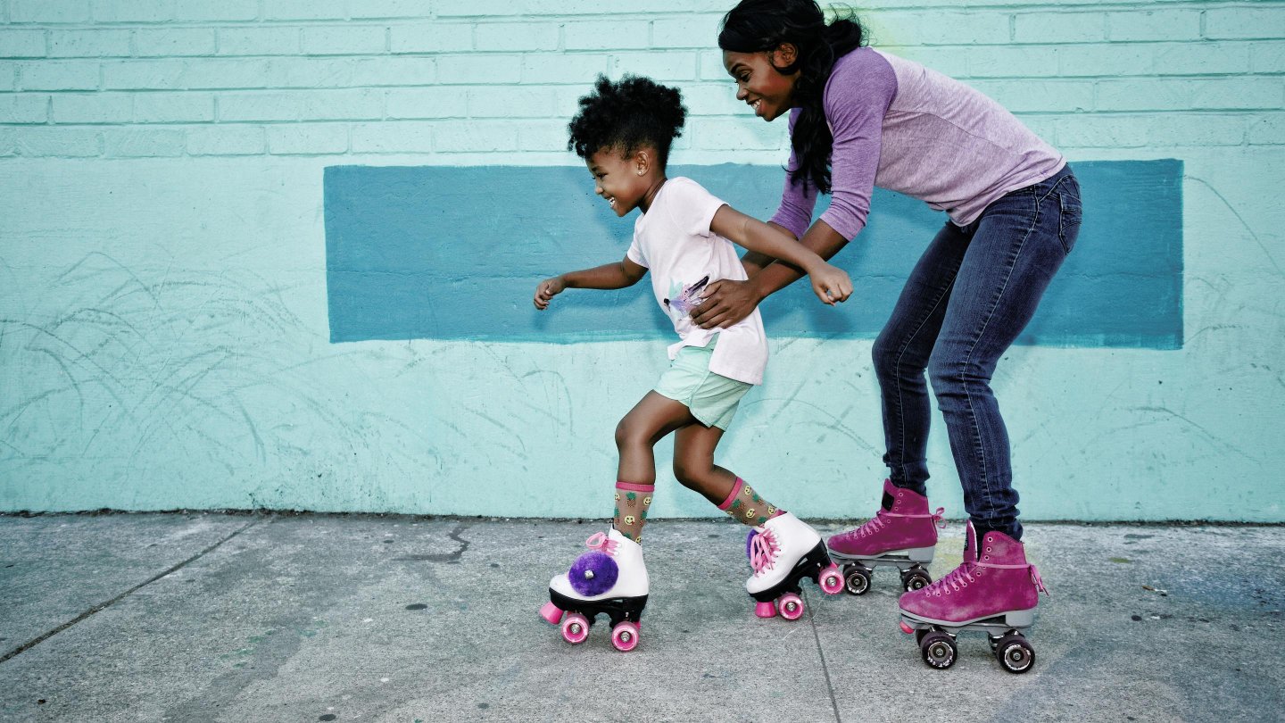 Black mother holding waist of daughter wearing roller skates