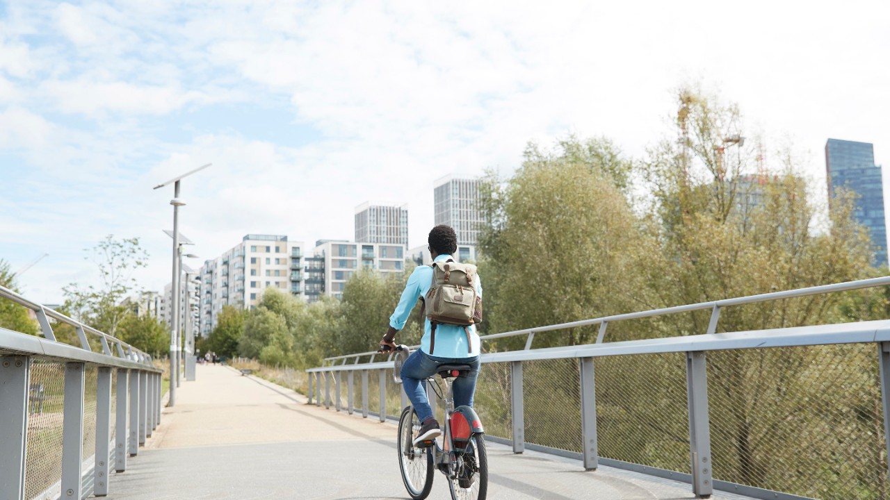 Girl riding a bike across a bridge toward a city.