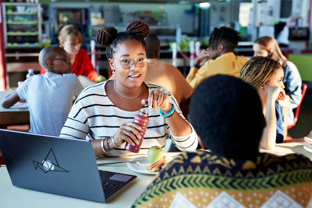 Young female students talking while enjoying lunch in cafeteria at community college