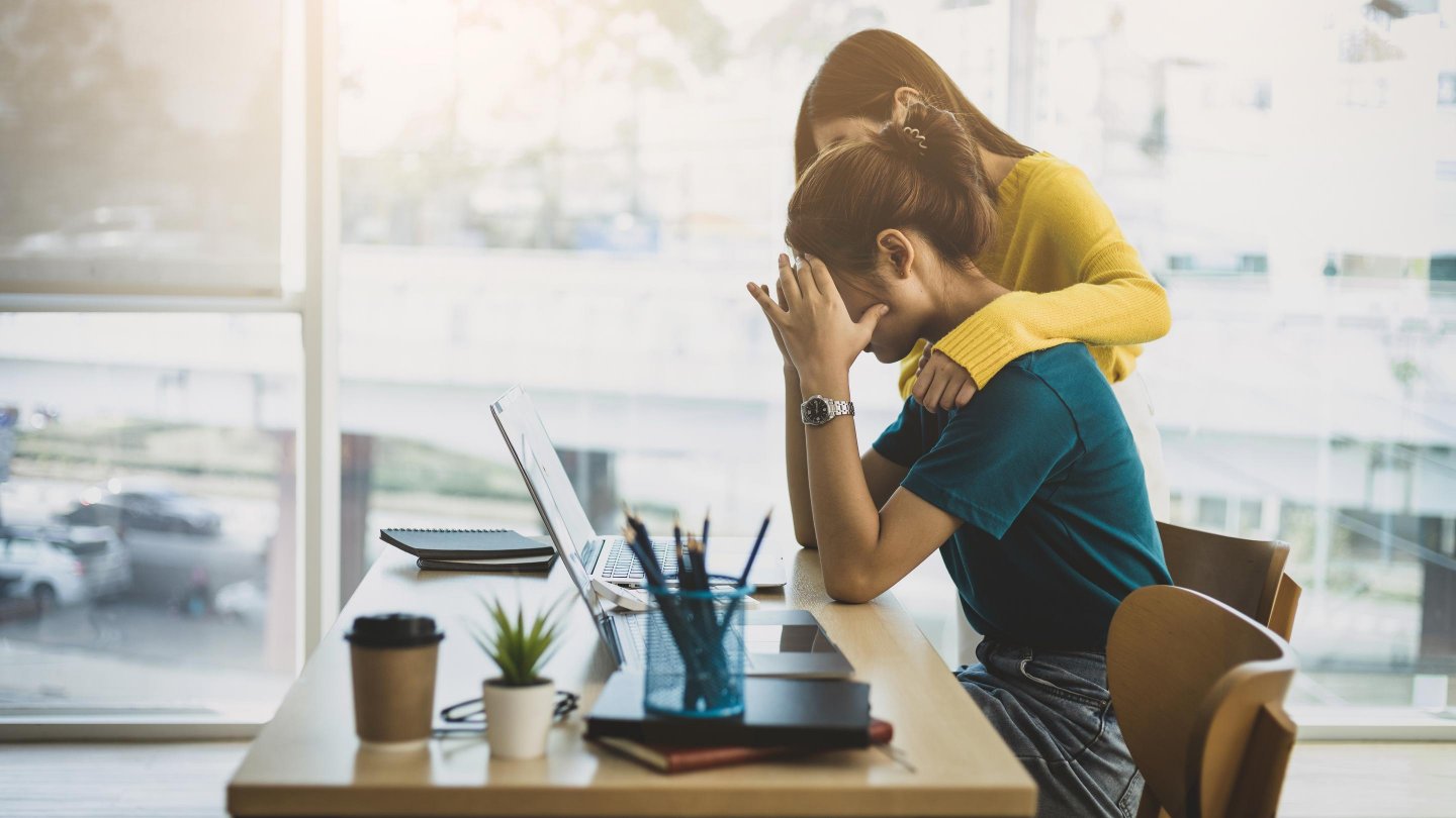 Coworker comforting stressed and discouraged woman in office.