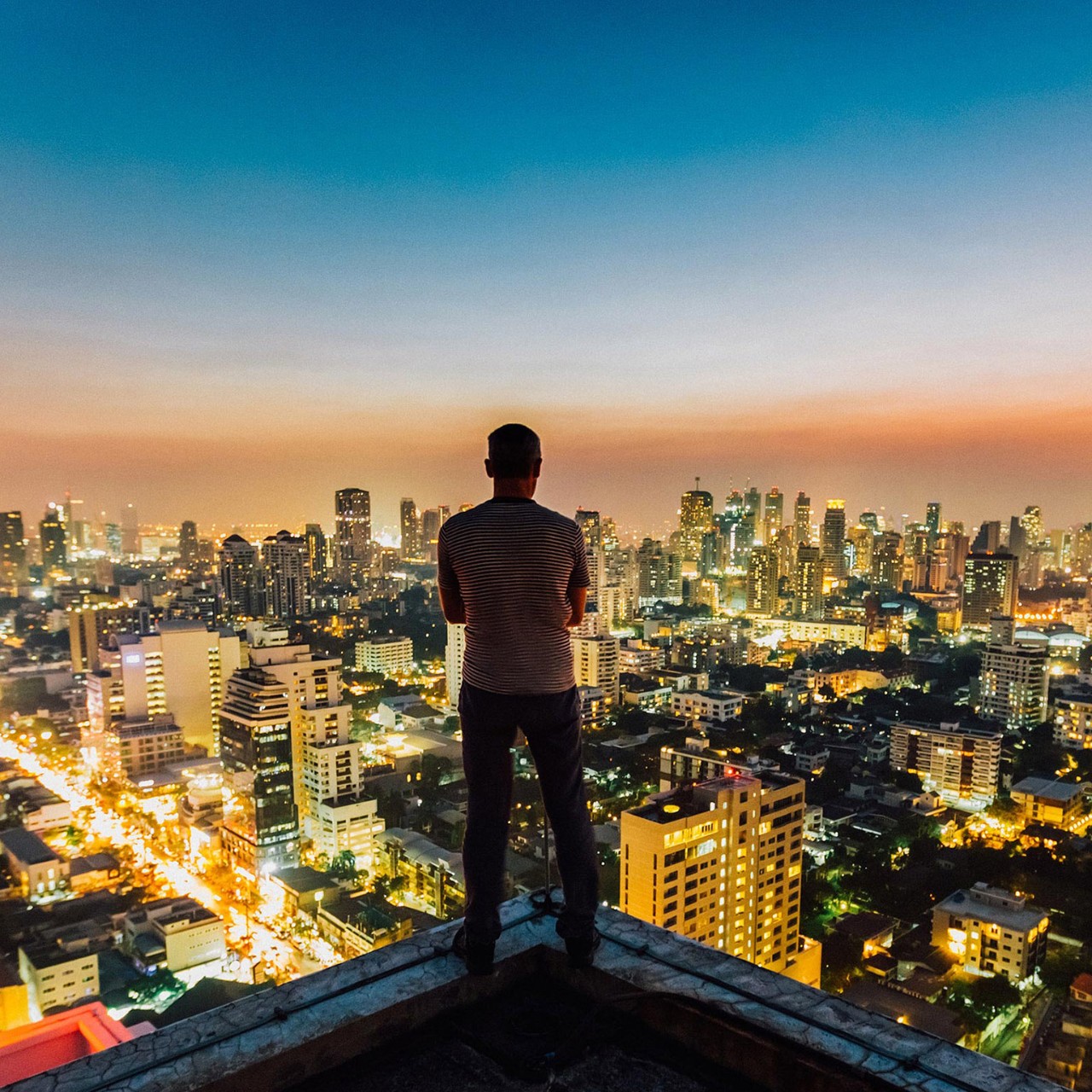 man standing on top of a skyscraper view of the Bangkok city skyline.