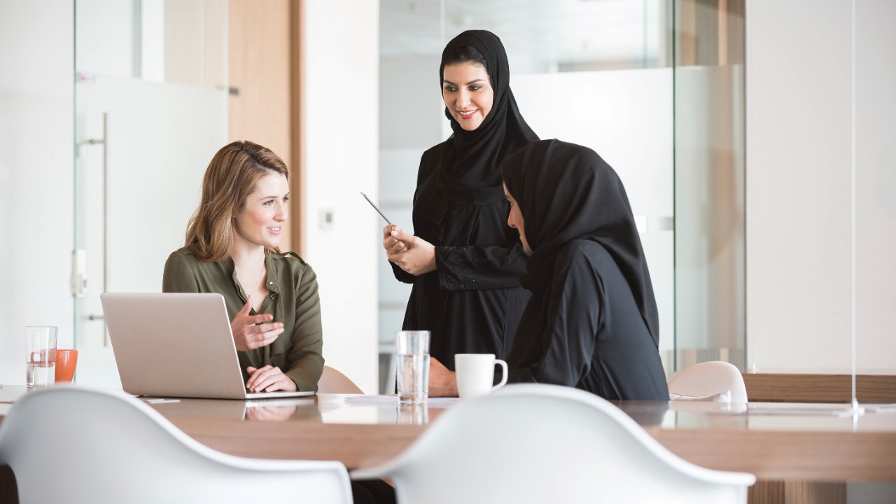 A photo of multi-ethnic businesswomen discussing in modern office in the Middle East. Multiracial Arab and Caucasian professional women are at conference table in modern middle eastern workplace.