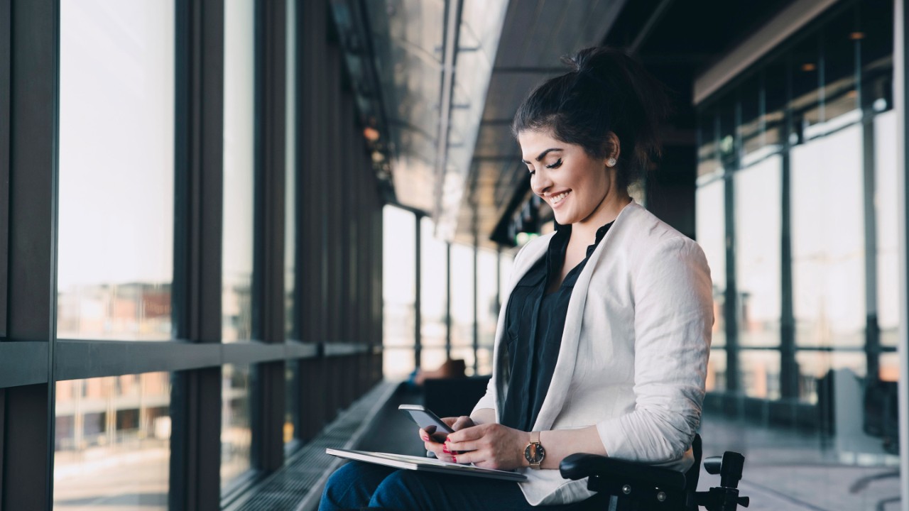 Smiling businesswoman with physical disability using smart phone in office corridor