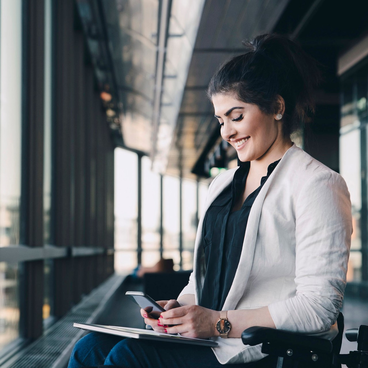 businesswoman in wheelchair using phone in front of windows