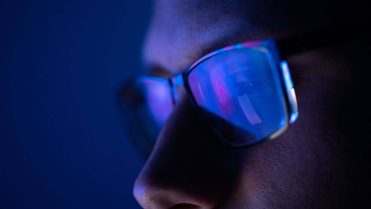 Close-up of a part of a male human face with eyeglasses in neon glow on a background of the vibrant colored liquid