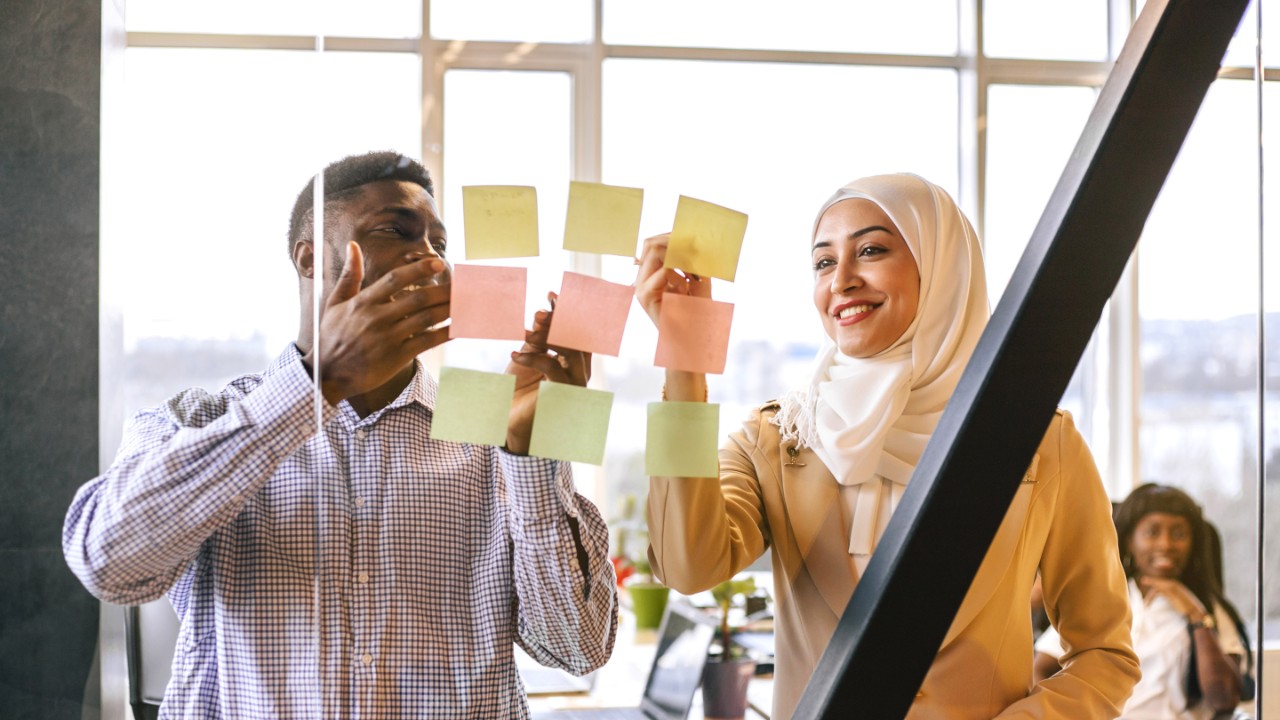 Multiracial teamworking. Black man and Muslim woman discuss their project with a help of pictures.