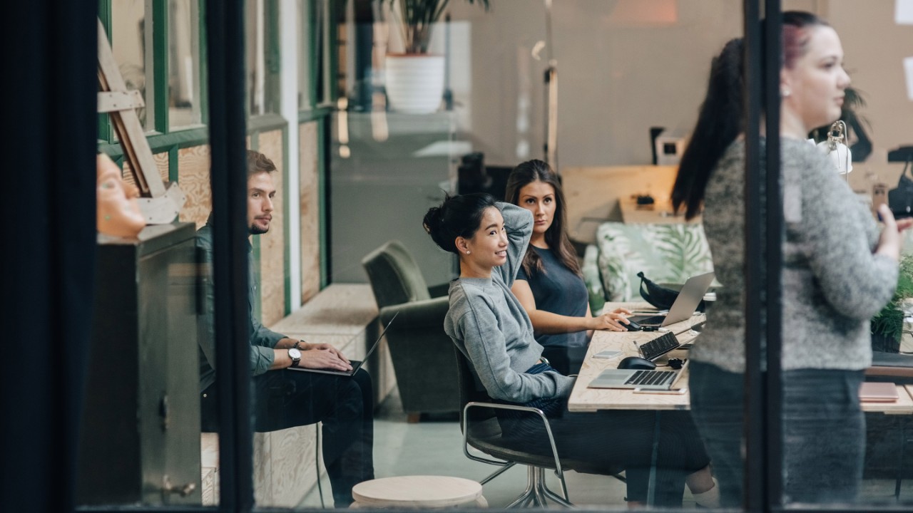 Businesswoman discussing with colleagues in meeting at office seen through glass wall