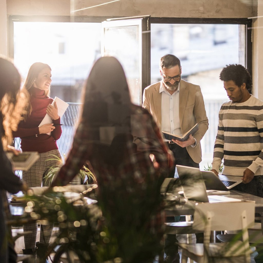 Group of multi-tasking creative people working on a meeting in the office. The view is through glass.